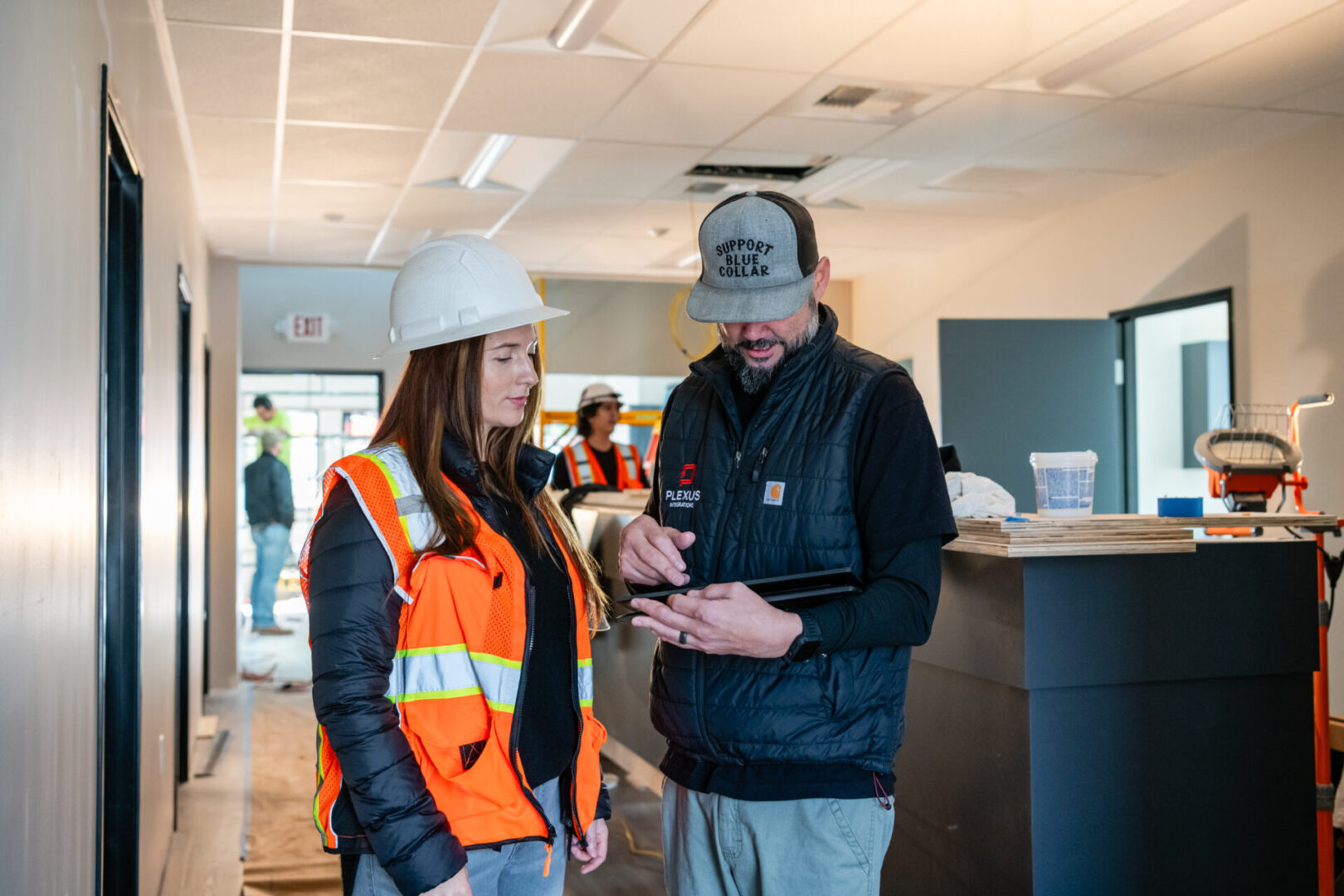 A man and woman in hard hats looking at something on a tablet.