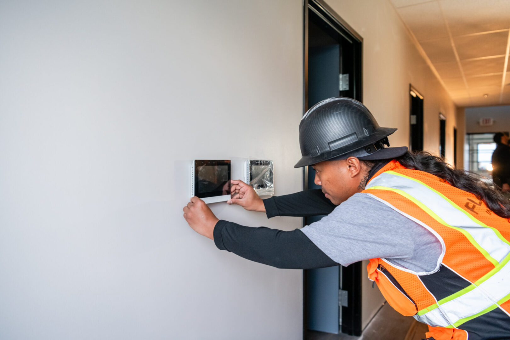 A man in an orange vest and hard hat working on the wall.